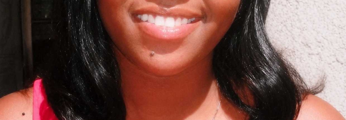 Young woman with black hair smiling outdoors while wearing a bright pink sleeveless top.
