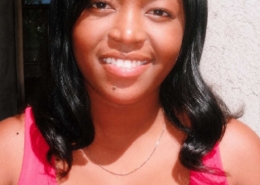 Young woman with black hair smiling outdoors while wearing a bright pink sleeveless top.