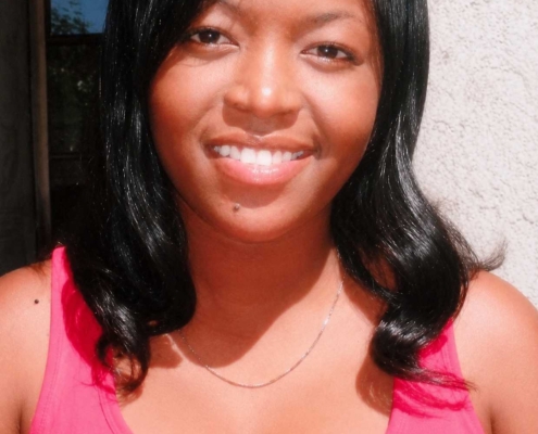 Young woman with black hair smiling outdoors while wearing a bright pink sleeveless top.